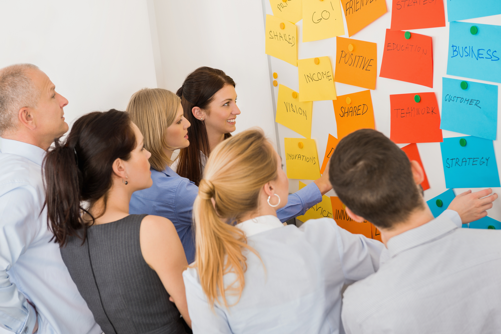  A group of people are brainstorming ideas in a meeting and writing them on sticky notes that they are attaching to a whiteboard.